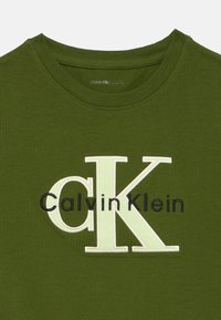 Oliwkowa bawełniana koszulka z okrągłym dekoltem, haftowanym logo "Calvin Klein" w bieli i czerni oraz gładką fakturą.