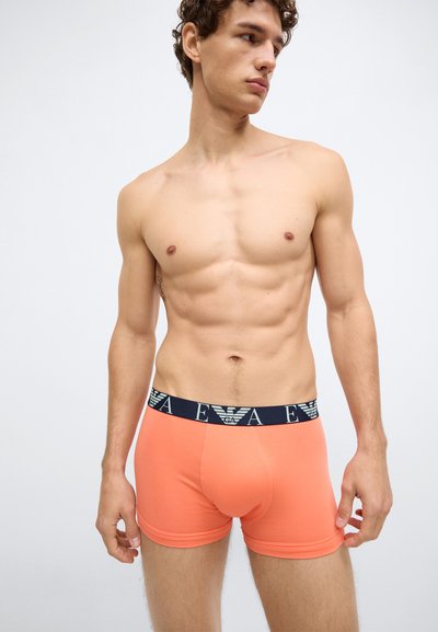 Boxers laranja feitos de tecido macio, com cós azul marinho com detalhes de logotipo branco, design ajustado e textura suave.