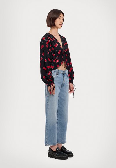 Svart kortermet bluse med rødt kirsebærmønster, knyttet i midjen, og lange ermer. Lys blå vide jeans med frynset hem. Svart platå-sko.