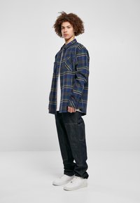 Blå rutete skjorte med lange ermer, kombinert med mørk denimbukser og hvite sneakers. Merkbare lommedetaljer på skjorten.