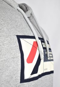 Sudadera gris con bolsillo tipo canguro, que presenta un gran parche gráfico multicolor, capucha con cordón y tejido texturizado.