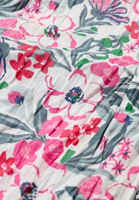 Blommig tyg med rosa och röda blommor samt gröna löv på vit bakgrund; texturen är mjuk med en lätt rynkig yta.