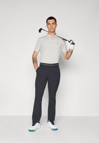 Szürke, rövid ujjú polo póló, gallérral, sötét nadrág, fehér golfcipő kék díszítéssel, a jobb kezében golfütővel.