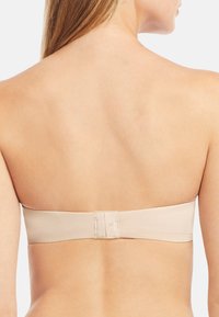 Nude bandeau-rintuli, jossa on sileä pinta; leveä nauha ja turvallinen takaklipsi; saumaton muotoilu sopii olkaimettomiin asuihin.