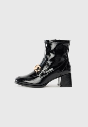 Black patent leather ankle boot with a square toe and heel. Features a gold buckle accent and stitched detailing along the upper.