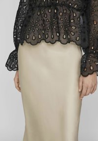 Svart spetsblus med blommönster och vågiga kanter, kombinerad med en slät, krämfärgad satinskjol. Strukturerade mönster på toppen.