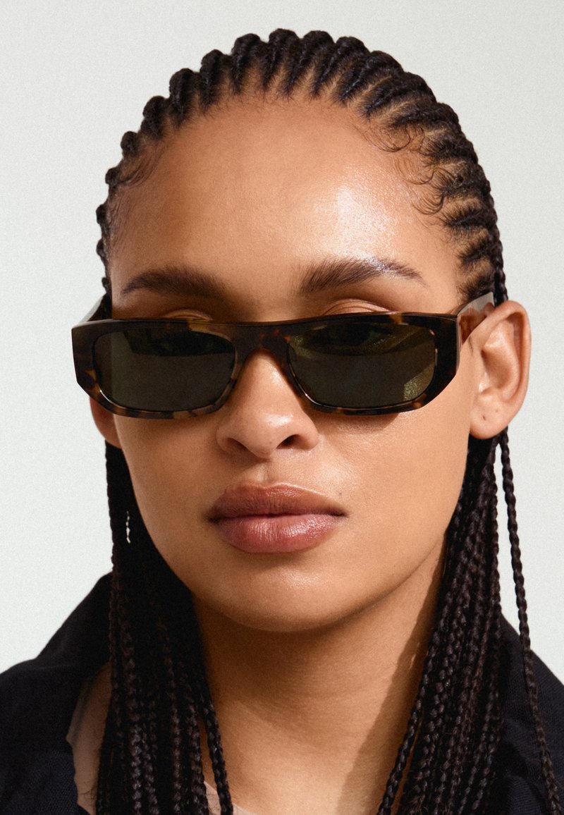 Lunettes de soleil écaille de tortue avec une monture rectangulaire et des verres foncés. Le design présente des bords angulaires et une finition brillante.