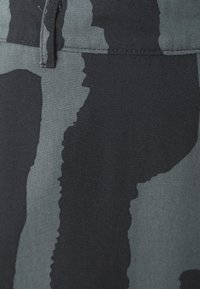 Tessuto con stampa camouflage in nero e grigio, dalla consistenza morbida. Presenta motivi irregolari e cuciture lungo i bordi verticali.