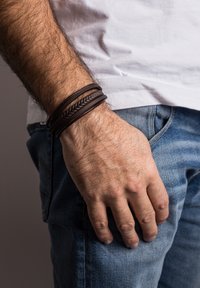 Brown leather bracelets, one braided, layered on a wrist. The hand rests on denim jeans, highlighting texture and contrasting colors.