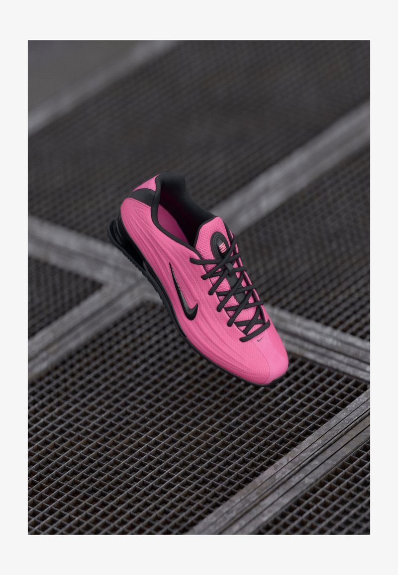 Scarpa sportiva Nike di un vivace colore rosa, con una superficie testurizzata, lacci neri e logo. Design elegante con una suola imbottita per il massimo comfort.