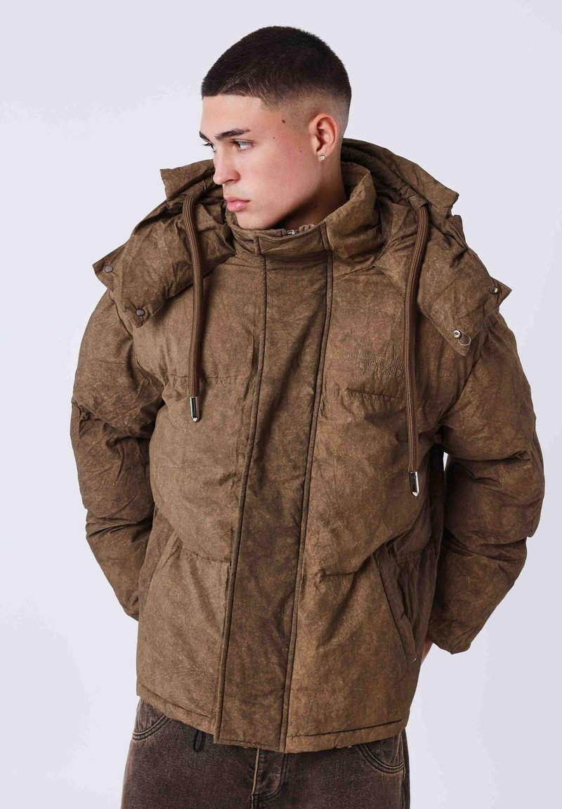 Chaqueta acolchada marrón con cuello alto, capucha y cordones ajustables. Presenta un material texturizado y dos bolsillos frontales con cierres de presión.