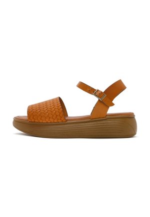 Sandali in pelle tan con tomaia intrecciata, punta aperta, cinturino alla caviglia regolabile e una spessa suola piattaforma marrone con scanalature orizzontali.