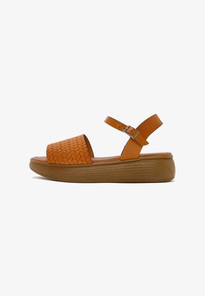 Braune Ledersandalen mit geflochtenem Obermaterial, offener Zehenpartie, verstellbarem Knöchelriemen und einer dicken braunen Plattformsohle mit horizontalen Rillen.