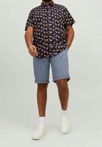 Camisa de manga corta azul marino con patrón de flamencos rosas, combinada con pantalones cortos claros enrollados y zapatillas blancas. Tejido suave, diseño casual.