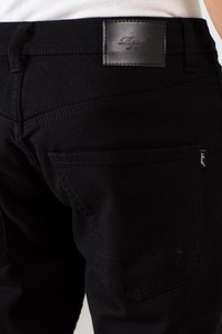 Pantalones de mezclilla negros con un parche de cuero en la cintura, costuras en el bolsillo trasero y un diseño de corte ajustado.