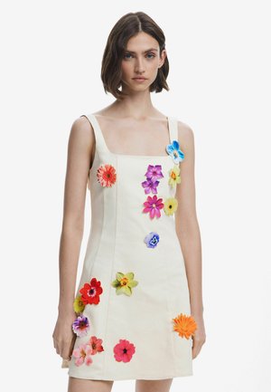 Floral-embellished cream dress with a square neckline, sleeveless design, and colorful flowers in various sizes attached throughout.