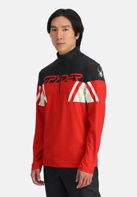 Pullover a maniche lunghe rosso e nero con zip a metà, caratterizzato da accenti bianchi e un logo Spider sulla spalla. Tessuto morbido, vestibilità atletica.