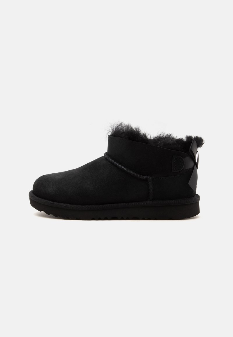 Bottine noire à cheville en daim souple avec doublure en peluche, semelle plate et détail ruban à l'arrière.