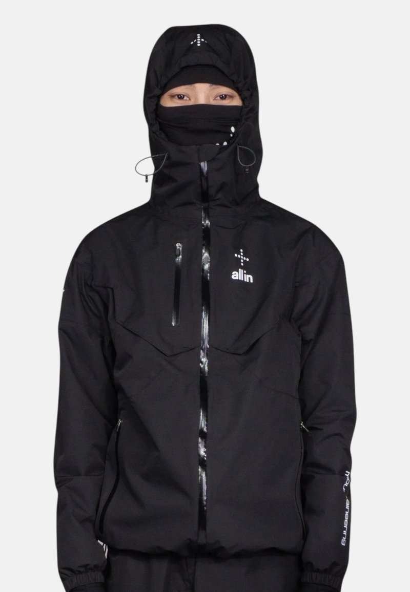 Veste noire imperméable avec poches zippées, une capuche ajustée, des cordons de serrage réglables et un logo sur la poitrine et la manche.