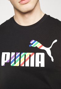 T-shirt noir avec un logo blanc audacieux "PUMA". Le logo comprend une silhouette de puma rayée multicolore, mettant en avant des couleurs vives.