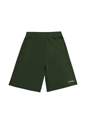 Mann trägt dunkelgrüne knielange Shorts, weiße Sneakersocken mit schwarzem Text und silberne New Balance Laufschuhe, steht vor einem einfarbigen Hintergrund.