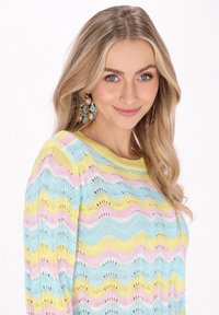 Pletený svetr s vlnitým vzorem v modré, žluté a růžové; má otevřenou pleteninu a kulatý výstřih. Lehké a volné přilnutí.
