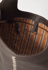 Brown leather tote bag interior featuring a striped fabric lining in brown, blue, and tan, with a zippered pocket and stitching detail.