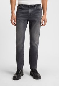 Jeans grigio scuro con un design classico a cinque tasche, caratterizzati da una leggera sfumatura e una vestibilità dritta. Indossati con stivali neri con lacci.