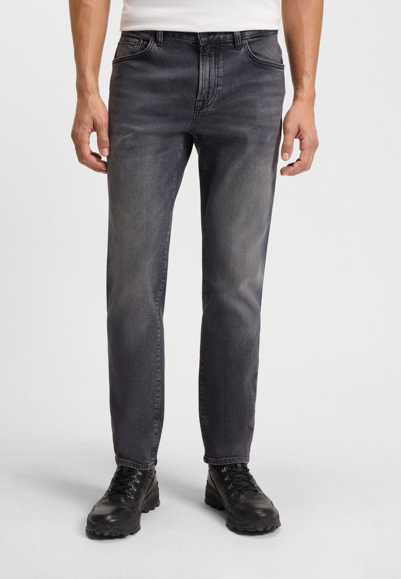Jeans grigio scuro con un design classico a cinque tasche, caratterizzati da una leggera sfumatura e una vestibilità dritta. Indossati con stivali neri con lacci.