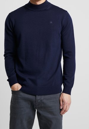 Navy blue turtleneck sweater made of a soft knit fabric, featuring long sleeves and a fitted design with ribbed cuffs and hem.