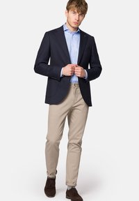 Granatowa marynarka na jasno-niebieskiej koszuli, zestawiona z beżowymi spodniami. Czarne buty dopełniają całość, charakteryzując się gładkimi strukturami i dopasowanym krojem.