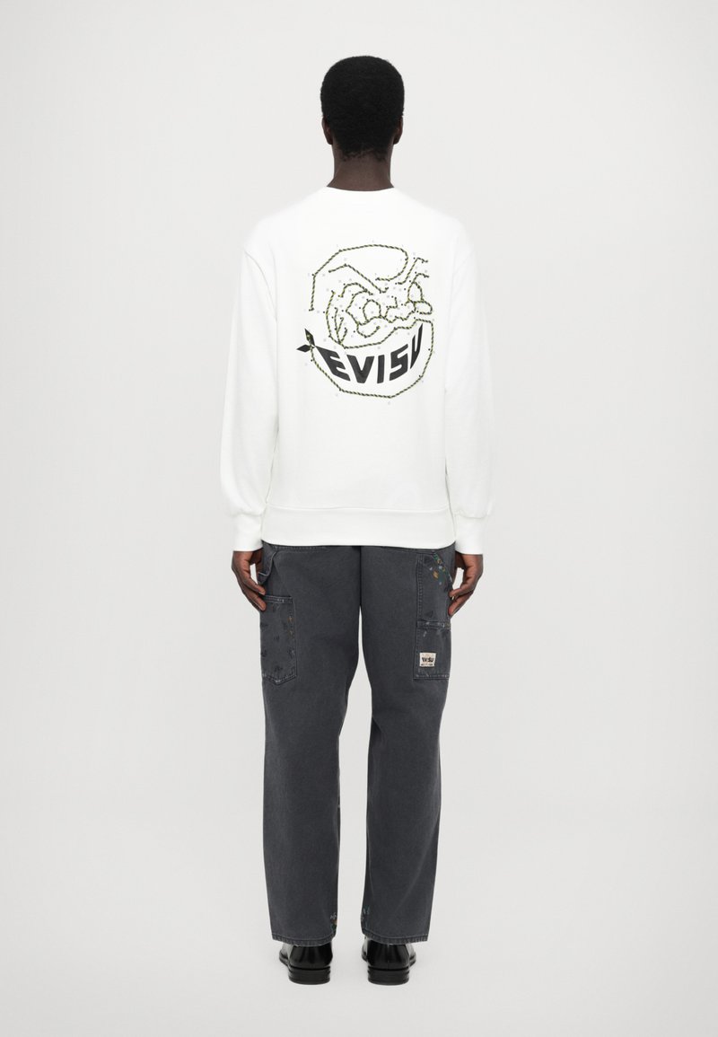 Vit sweatshirt med "EVISU"-logotyp och grafisk design på baksidan, kombinerad med mörkgrå cargobyxor med lappar och fickor.