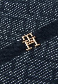 Tejido navy con rayas blancas texturizadas, que presenta un acento de logo metálico dorado. El material parece suave con un patrón tejido.
