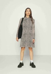 Vestido de estampa de leopardo com mangas longas, gola e saia fluida; combinado com uma mala preta e sapatos pretos robustos.