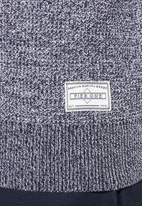 Pull en maille gris et marine avec un motif texturé. Comprend une étiquette indiquant "Pier One" cousue sur la partie inférieure.