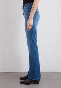 Flared blauwe jeans van denim, met een middelhoge tailleband, gestikte zakken en een soepele textuur, gecombineerd met zwarte leren laarzen met hak.