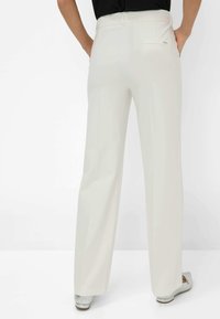 Lichtcrème wijde broek met een gladde textuur en een achterzak. De tailleband is iets verhoogd. Geen zichtbare sluitingen.