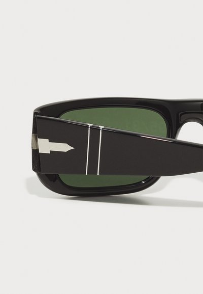 Ochelari de soare negri cu lentile verzi, având un design unghiular unic și detalii argintii pe mâner, inclusiv un model în formă de săgeată.