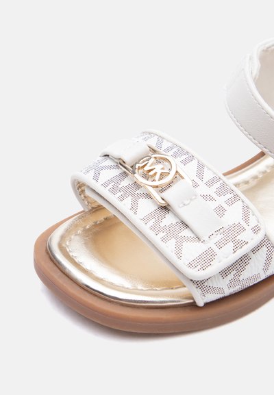 Λευκό σανδάλι με ιμάντα από υφαντό ύφασμα, αγκράφα με λογότυπο Michael Kors σε χρυσό τόνο, μαξιλαρωτό μεταλλικό χρυσό πάτο και καφέ σόλα.