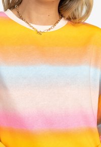 Sudadera de gradiente multicolor con franjas en naranja, rosa y azul. Tejido suave y escote barco con un ribete blanco. Collares de cadena dorados visibles.