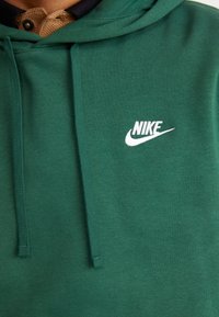 Zaļš kapuce ar mīkstu audumu, tajā skaitā priekšējā kabata. Baltais Nike logs izšūts kreisajā krūtī. Kapuces aukliņas.