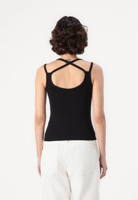 Black tank top with a fitted design, featuring thin straps and a cross-back detail. The fabric appears smooth and stretchy.