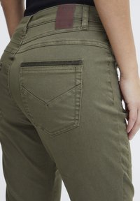 Olijfgroene denimbroek met een aansluitende pijp, voorzien van een middelhoge taille, achterzakken met schuine naden en een bruin leren merklabel.