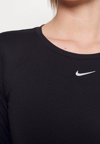 Maglietta sportiva nera con scollatura tonda, caratterizzata da un motivo testurizzato e un piccolo logo Nike bianco sul petto.