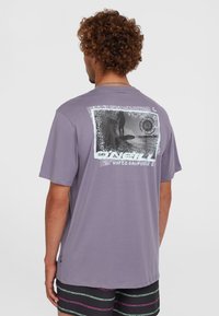 Paarse t-shirt met korte mouwen met een grafische print op de achterkant, waarop een surfer is afgebeeld. Gemaakt van zacht materiaal met een relaxte pasvorm.