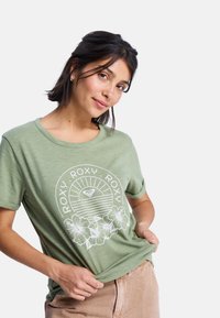 T-shirt vert à manches courtes avec un design floral blanc et un texte de marque. Texture douce avec une coupe décontractée et un col rond.