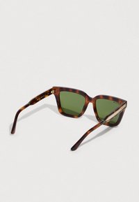 Τετράγωνα γυαλιά ηλίου με σκελετό από θαλάσσια χελώνα, πράσινους φακούς και λεπτά μπράτσα με γεωμετρικό σχέδιο στην εσωτερική πλευρά.