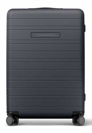 Valise rigide gris foncé avec rainures horizontales, quatre roues double pivotantes et une poignée supérieure.