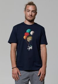 T-shirt en coton bleu marine avec un motif d'astronaute tenant des ballons de planète multicolores. Manches courtes, col rond.