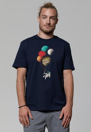 Marineblauwe katoenen t-shirt met een grafisch ontwerp van een astronaut die meerkleurige planetenballonnen vasthoudt. Korte mouwen, ronde hals.